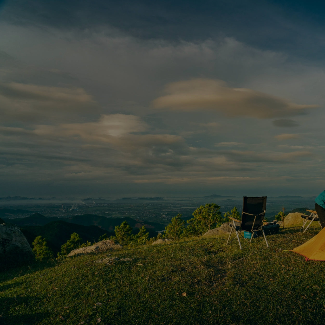 Camping tent and chairs overlooking scenic mountain valley at sunset