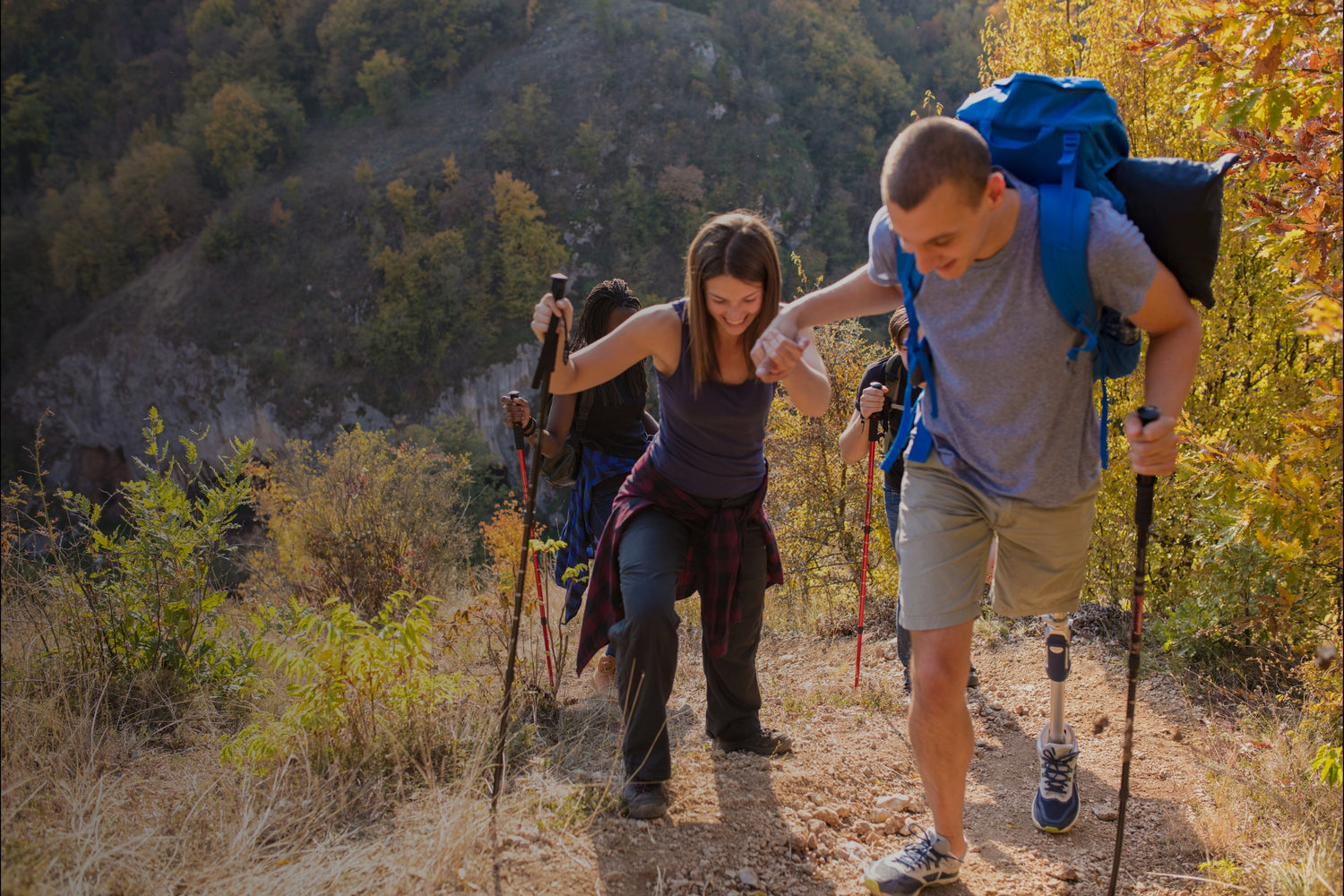 Couple hiking uphill mountain trail with trekking poles and large blue backpacks