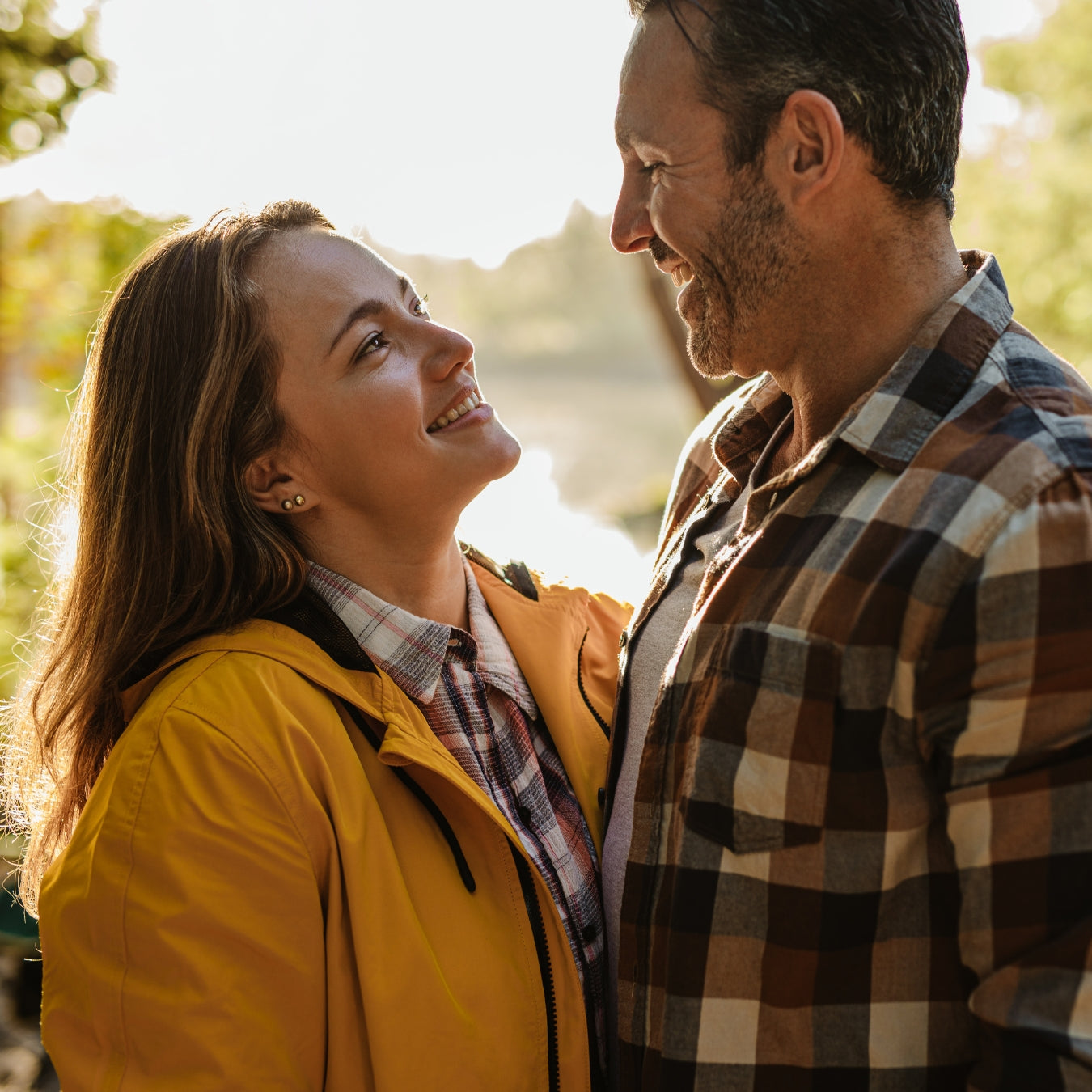 Man and woman smiling at each other outdoors with a blurred natural background