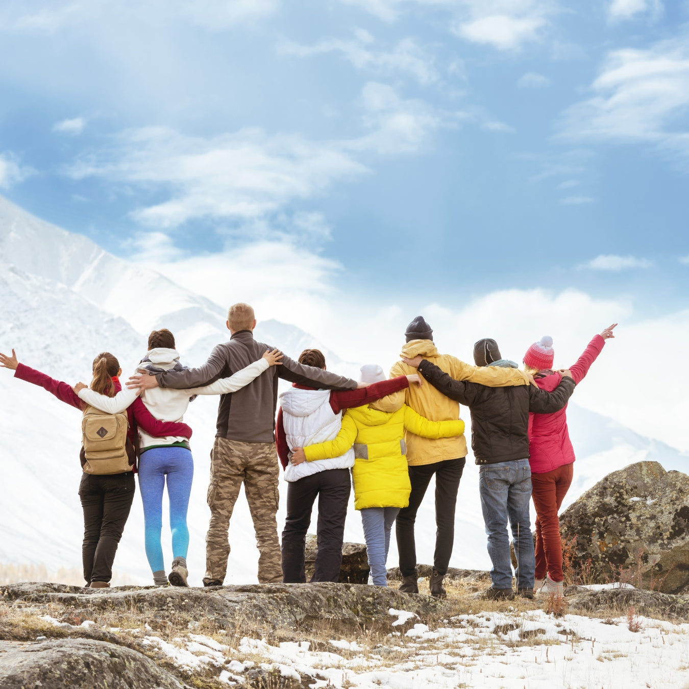Friends celebrating together at snowy mountain summit with arms raised high