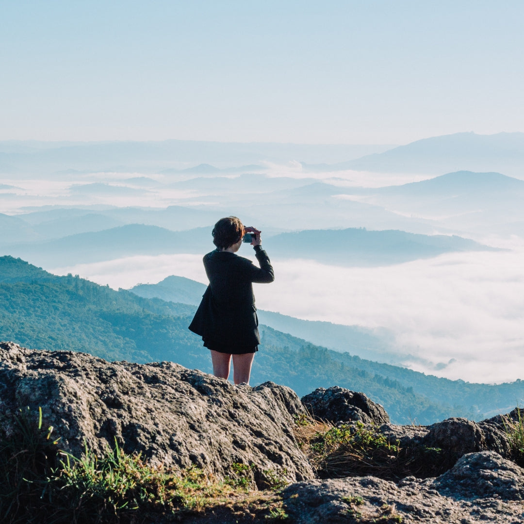 Person taking a photo of a mountainous landscape with clouds below